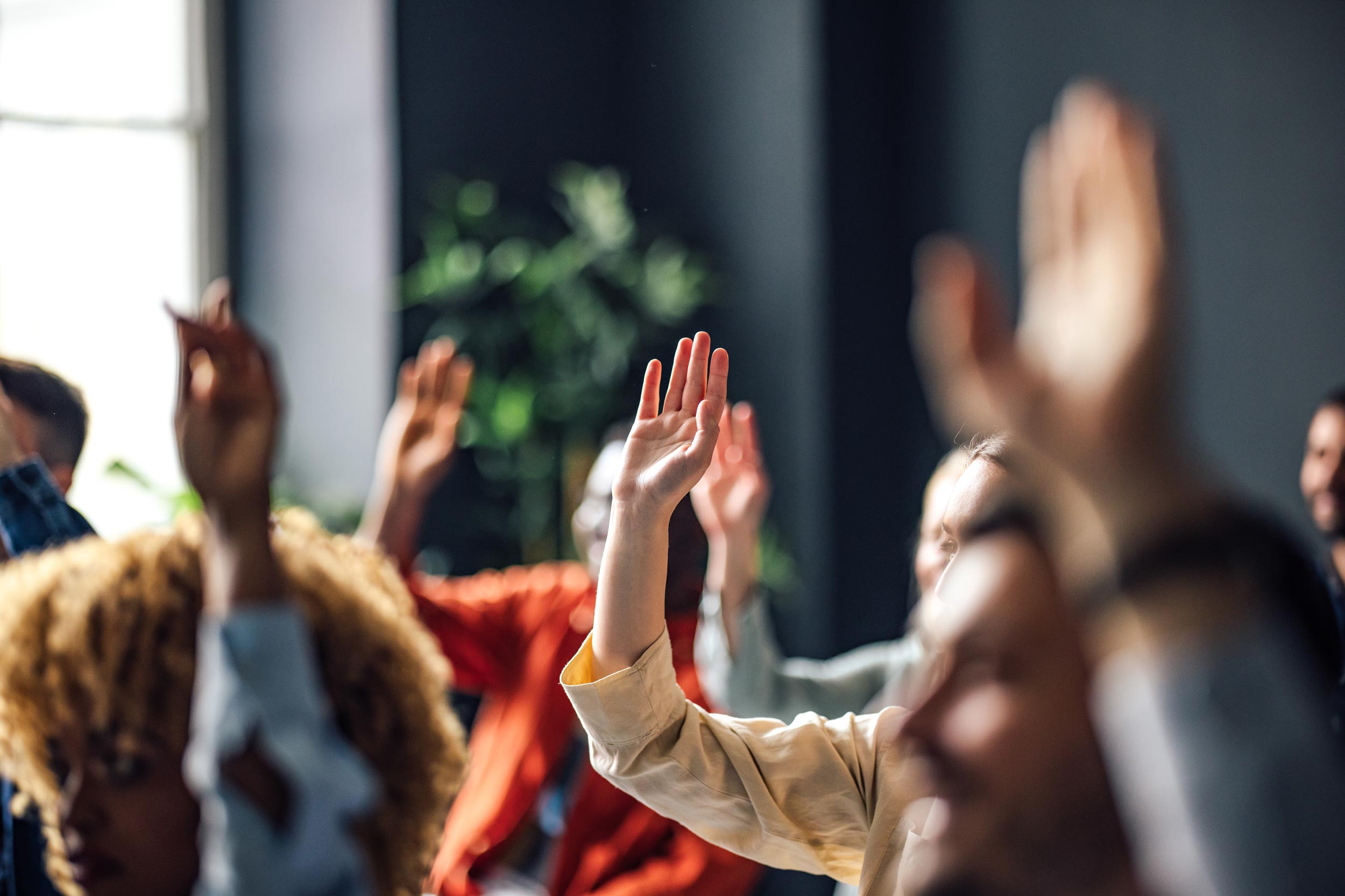 Different people in a room raising their hands for voting.